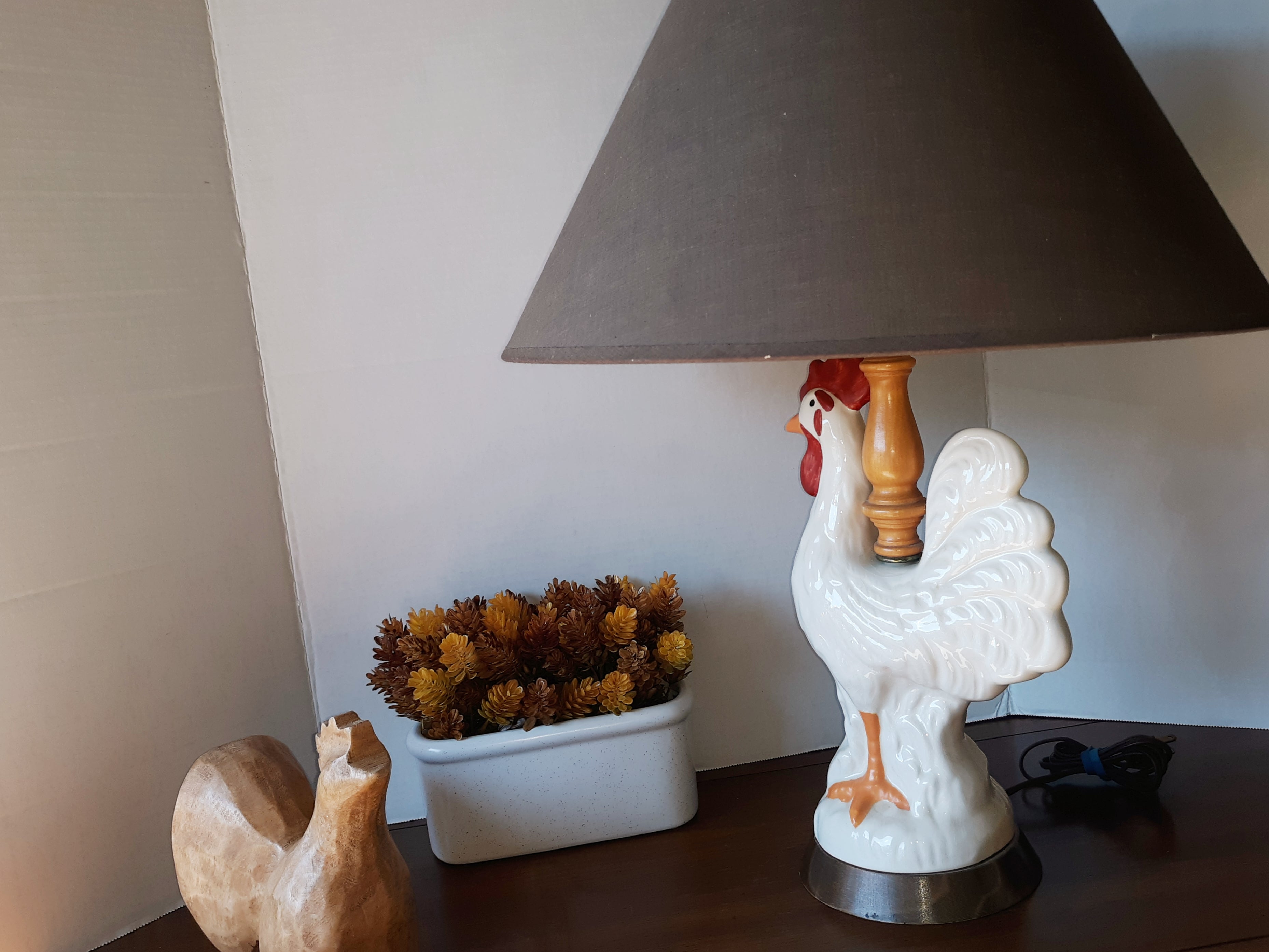 Small rooster lamp with a hand carved rooster beside the lamp in the background a white pot with fall colors accents the look